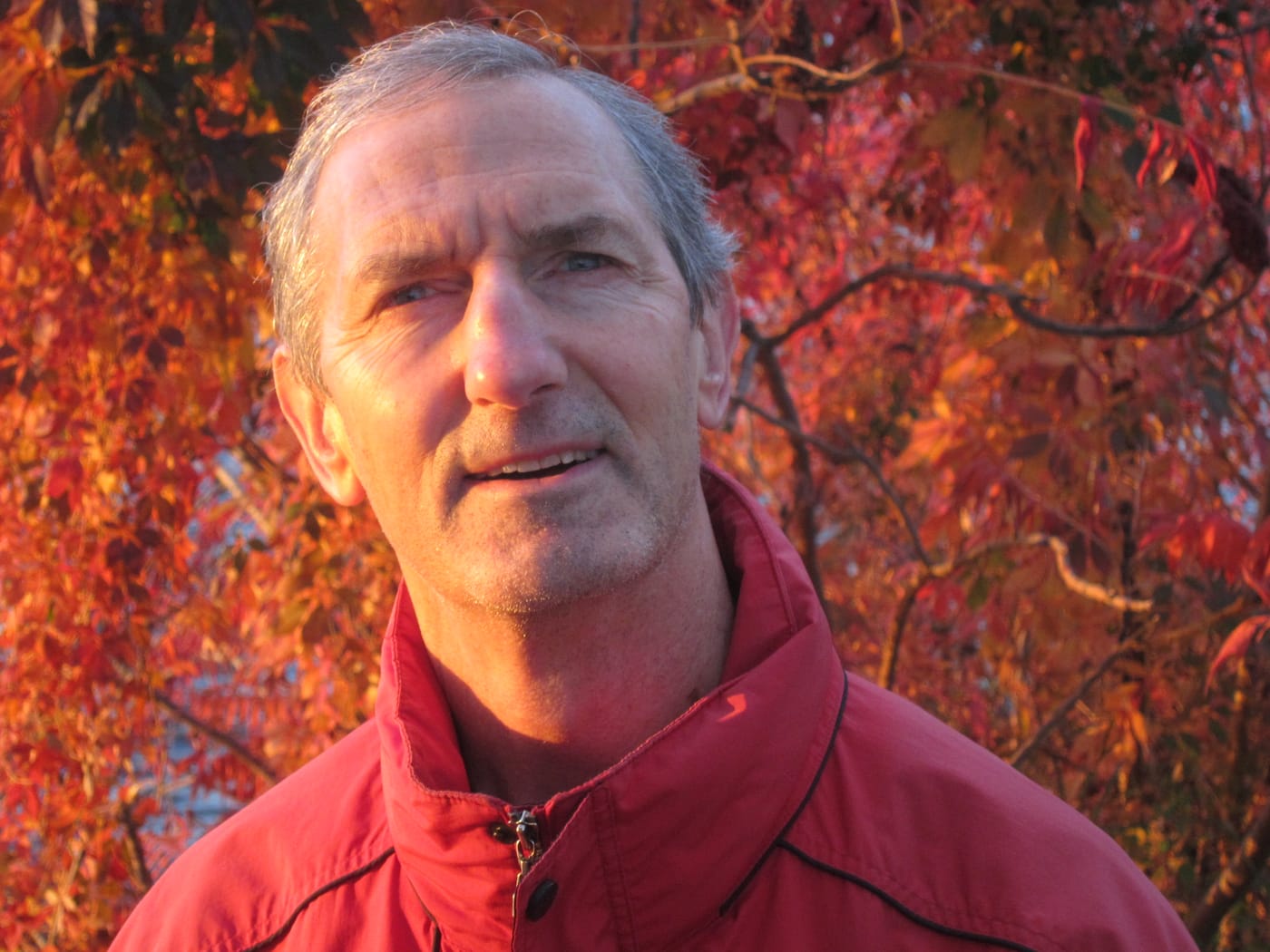 Portrait of Gary J. Kirchner in a red jacket in front of autumn leaves